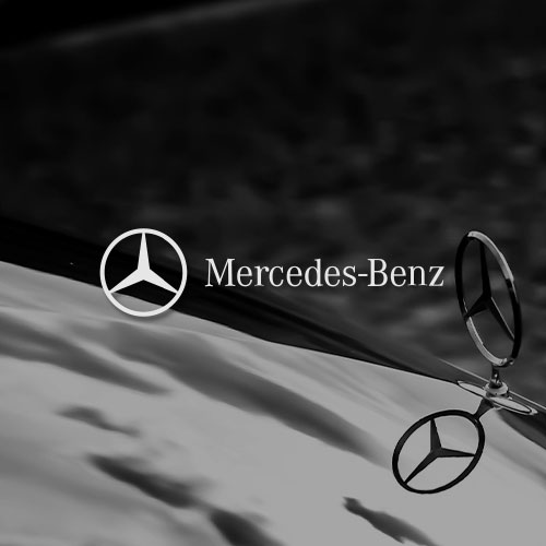 Schwarz-weiß Bild einer Motorhaube mit dem Mercedes-Stern. Mittig im Bild wird das Mercedes-Benz Logo dargestellt.