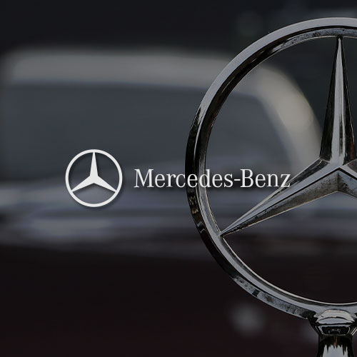 Nahaufnahme eines Mercedes-Benz-Sterns auf einem Auto. Mittig im Bild wird das Mercedes-Benz Logo dargestellt.