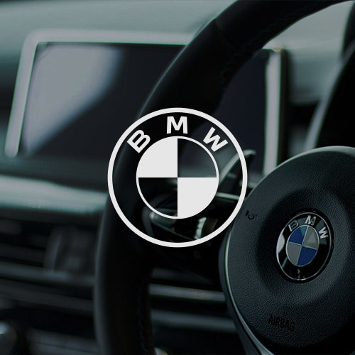 Lenkrad in einem Auto. Mittig im Bild wird das BMW Logo dargestellt.
