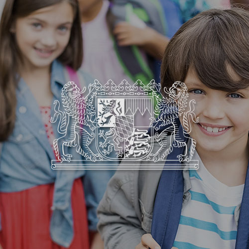 Lächelnde Schulkinder. Mittig im Bild wird das Bayrische Staatsministerium Logo dargestellt.