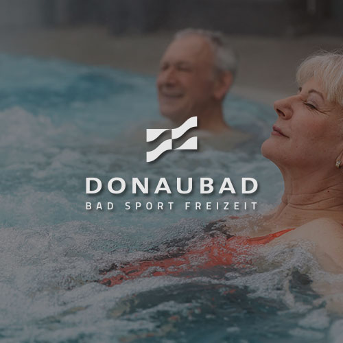 Eine Frau und Mann sitzen in einem Whirlpool. Mittig im Bild wird das Donaubad Logo dargestellt.