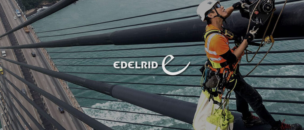 Arbeiter auf einer Straßenbrücke über einem großen Fluss. Mittig im Bild wird das Edelrid Logo dargestellt.